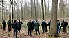 Eine Gruppe von Menschen steht in einem Waldstück. Es ist Winter, die Bäume tragen kein Laub.